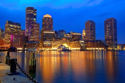 Boston\'s skyline glows at sunset, reflecting off the water at Fan Pier.