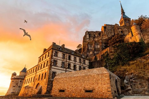 Seagulls flying over dramatic sunset in Mont Saint-Michel