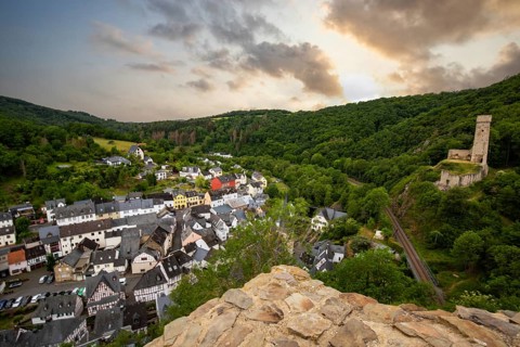 Landscape of a half-timbered village on a river, surrounded by hills and a castle. Beautiful nature