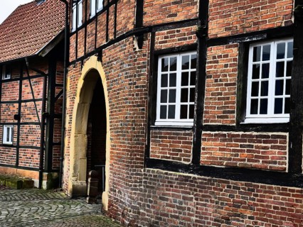 A close-up of a half-timbered house with brick walls and white windows, next to an archway, asbeck,