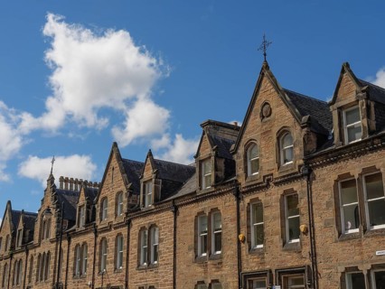 Row of historic buildings with pointed gables and stone facades under a blue sky in a cityscape,