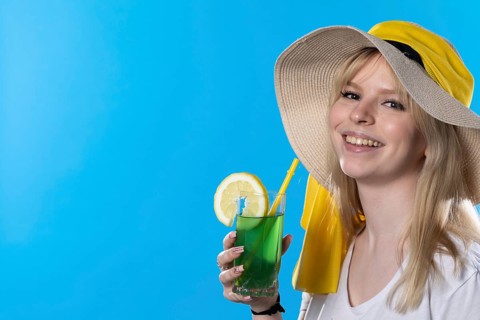 A teenager with an alcoholic drink in her hand and a large hat basks in the summer sun