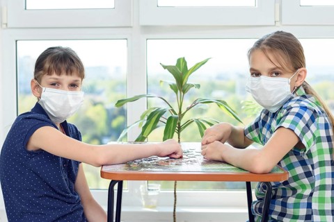 Two girlfriends in medical masks play puzzles and looked into the frame