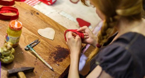 Brown-haired woman manufacturing heart-shaped red purses on the wooden table