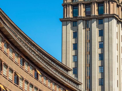 Modern building with a striking facade and a skyscraper in the background under a clear blue sky,