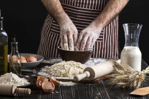 A handful of flour with egg on a rustic kitchen. Against the background of men's hands knead the