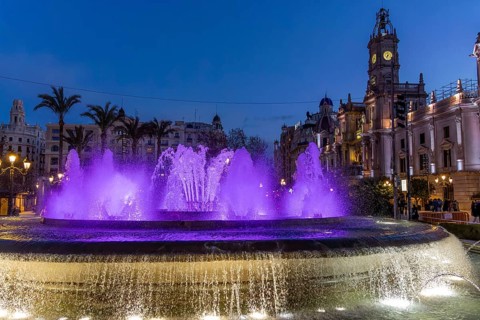 Night photo with purple illuminated water round fountain and blue sky in the centre of the old town