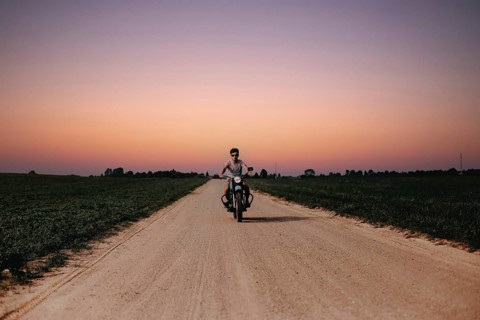 Rider on a motorcycle advances along a rural road during sunset, creating a serene atmosphere