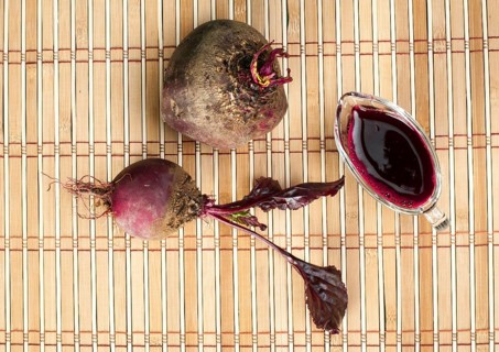 Red beets with leaves and jug with juice on wooden base