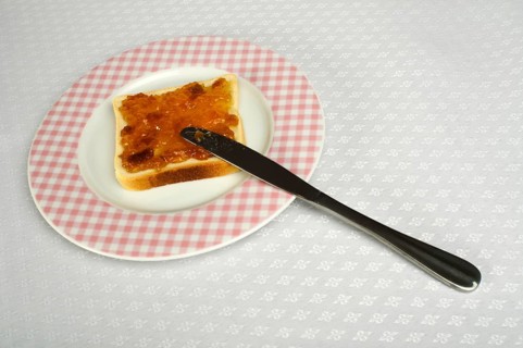 Spread jam on bread with knife. Pink checkered plate