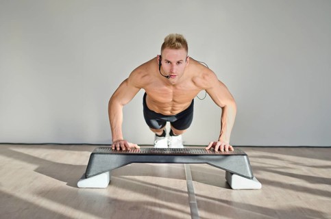 Young aerobics male coach shirtless leaning on step teaching class