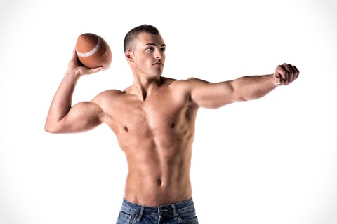 Handsome, athletic young man shirtless, throwing american football ball, isolated on white