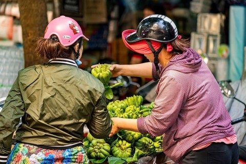 Two woman trading green fruits on Krong motorbikes in an urban environment, woman selling fruits in