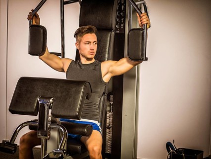 Muscular young man, training pecs on gym cable machine