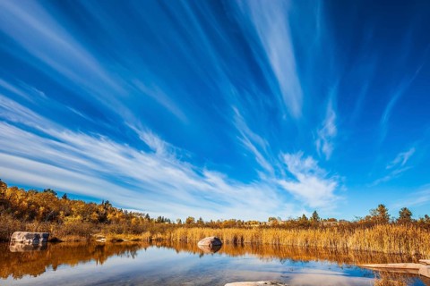 Cirrus clouds are reflected in the Winnipeg River. Wonderful autumn day. Old Pinawa Dam Park. The