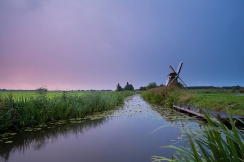 Charming windmill by river at rainy sunrise, Holland