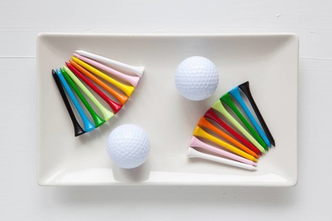 White ceramic dishes with golf balls and wooden tees on over white background, rectangle dish