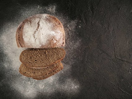 Sliced homemade sourdough rye bread with rye flour on black textured background. Top view or