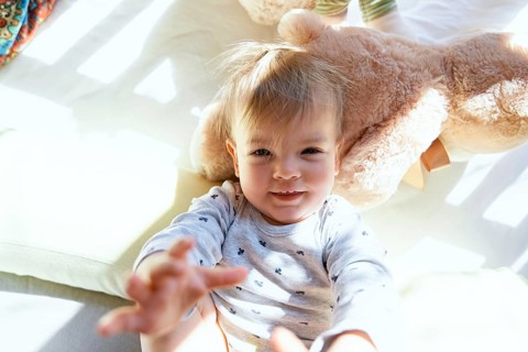 Small child lies in a wooden crib on a large teddy bear.