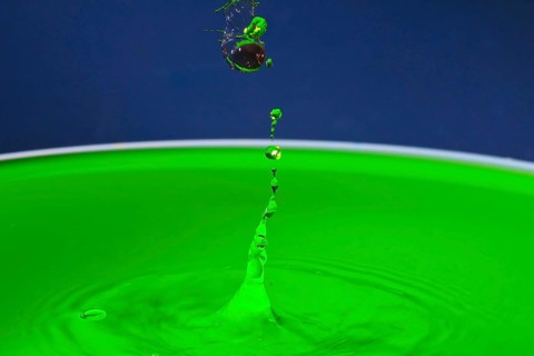 Green liquid splashes in a dynamic moment against a blue background, water droplets, collision,