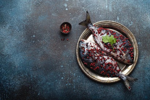Two raw fishes dorado seasoned in pink peppercorn ready to be cooked laying on rustic metal plate
