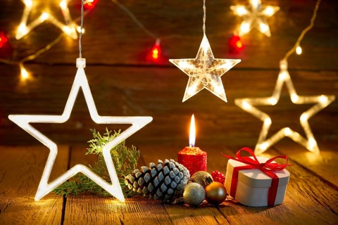 A candlelit wooden table with gifts, pine cones, and star lights