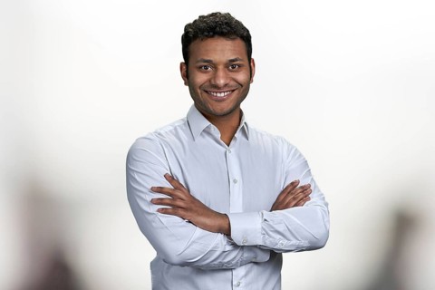Handsome smiling man with crossed arms looking at camera. Portrait of indian businessman on blurred