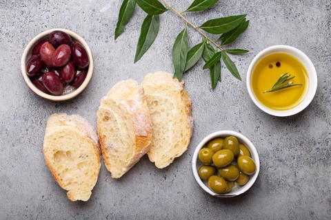 Slices of fresh ciabatta, green and brown olives, olive oil with rosemary, olive tree branches on