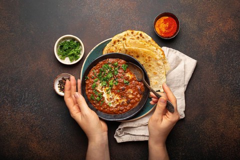 Female hands holding a bowl and eating traditional Indian Punjabi dish Dal makhani with lentils and
