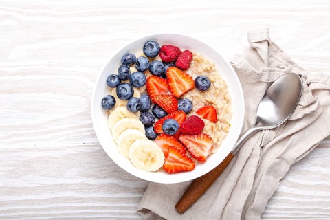 Oatmeal porridge with fruit and berries in bowl with spoon on white wooden background table top