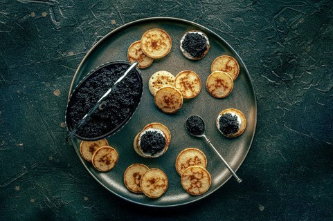Blinis with black caviar and cream cheese, overhead flat lay shot on a black background, mini