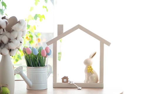 Key and tiny house of cozy home with Easter decor with rabbit and eggs on table of kitchen.