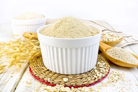 Oat flour in white bowl, oatmeal and bran in a spoon, stalks of oats, napkin against the background