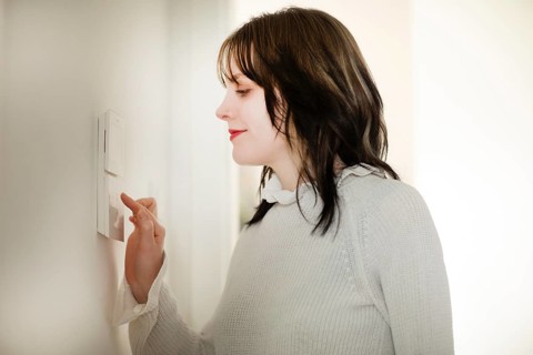 Woman operates a smart switch on the wall, save energy, environmentally friendly