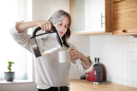 Woman pouring water into a cup in a bright kitchen with kettle, energy-saving, environmentally