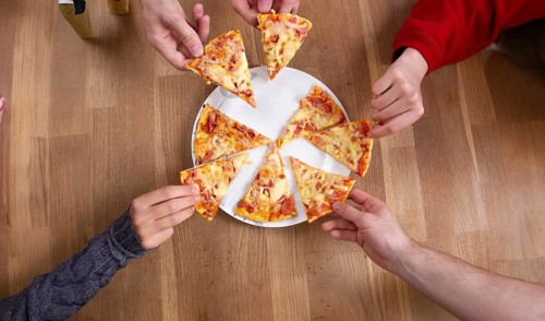 Multiple hands taking slices from a pizza placed on a wooden table