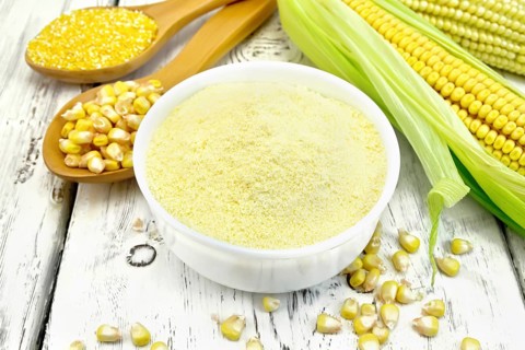 Flour corn in a bowl, groats and grain maize in the spoons, cobs on the background of wooden boards