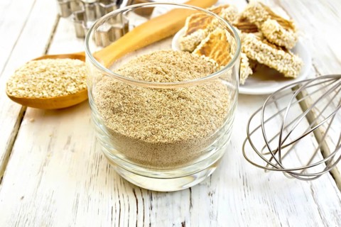 Sesame flour in a glass, a spoon with sesame seeds, cookie cutters and a mixer, biscuit on the