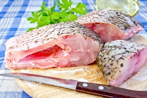 Bream raw sliced pieces on a circular board, parsley, vegetable oil, knife on blue linen tablecloth