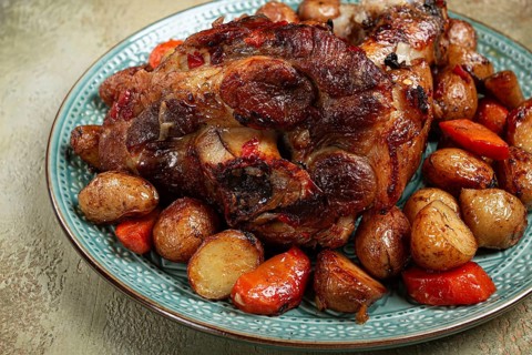 Pork knuckle baked with vegetables, new potatoes, on a plate, homemade, no people