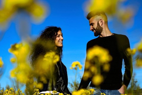 Portrait of a happy couple smiling holding hands looking at each other in a field of flowers in