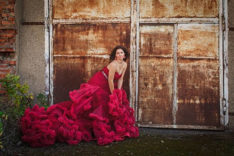 Woman in cloudy red dress is posing over rust wall. Fashion portrait without retouch, only make up