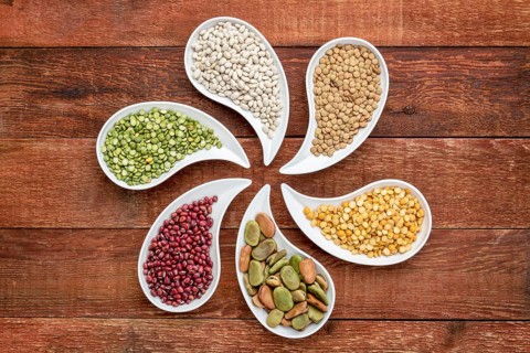 Variety of beans, lentils and pea in teardrop shaped bowls against rustic wood, top view