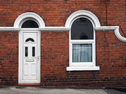White front door and window of a typical old brick british terraced house with white decorative