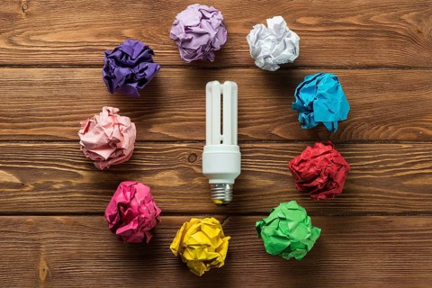 Lightbulb placed in circle of multiple crumpled paper balls on wooden table as means of searching