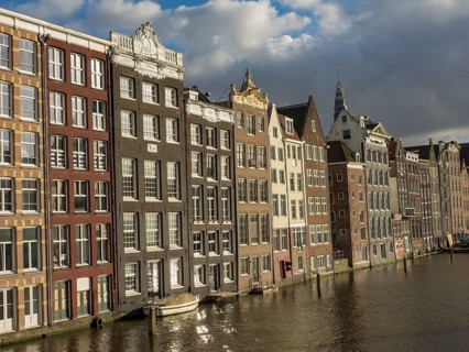 Row of historic canal houses on the waterfront with reflection and blue sky with clouds, amsterdam,