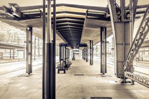 Covered platform in an empty modern railway station in sepia colour with striking metal structure,