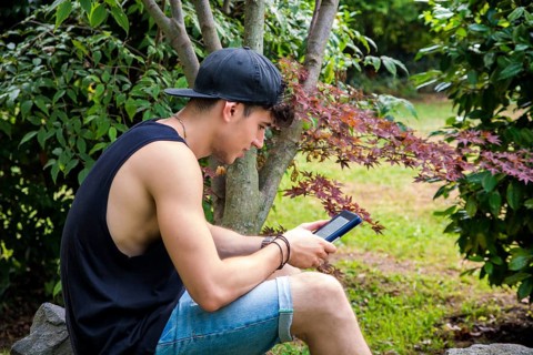 Smiling Young Handsome Man, Reading on Ebook Reader or Holding a Tablet Computer, Relaxing on