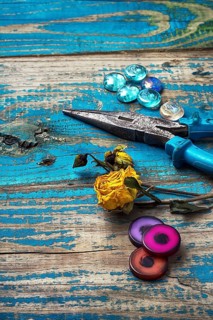 Beads, pliers, and other needlework accessories on outdated turquoise wooden background
