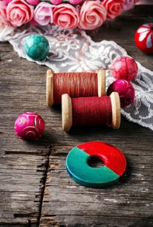 Beads and spool of thread, piece of lace on textured wooden background